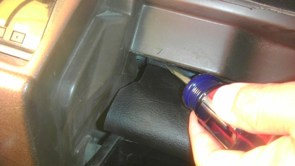 Hand using a screwdriver to pry open a black dashboard panel in a 1985 Toyota 4Runner
