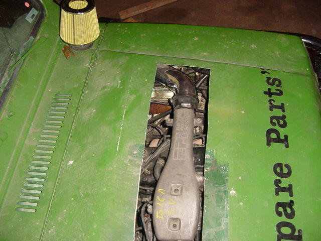 Engine intake tube and cone air filter visible through a cut hole in a green hood