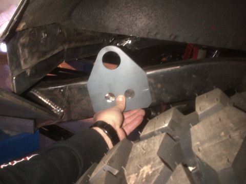 1985 Jeep CJ7 - A hand holds a metal bracket against the frame of a vehicle, near a large tire.