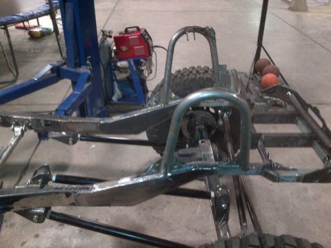 1985 Jeep CJ7 - The frame of a Jeep CJ is visible, modified with a roll cage and a spare tire mounted. A welding machine is also present in the background.