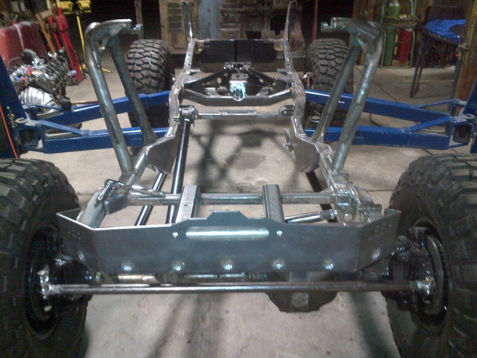 Jeep CJ frame, suspension, and tires in a workshop. The frame appears to be modified or under construction