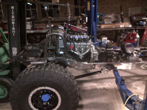 1985 Jeep CJ7 - A Jeep CJ frame is suspended on a lift, undergoing an engine installation in a workshop.