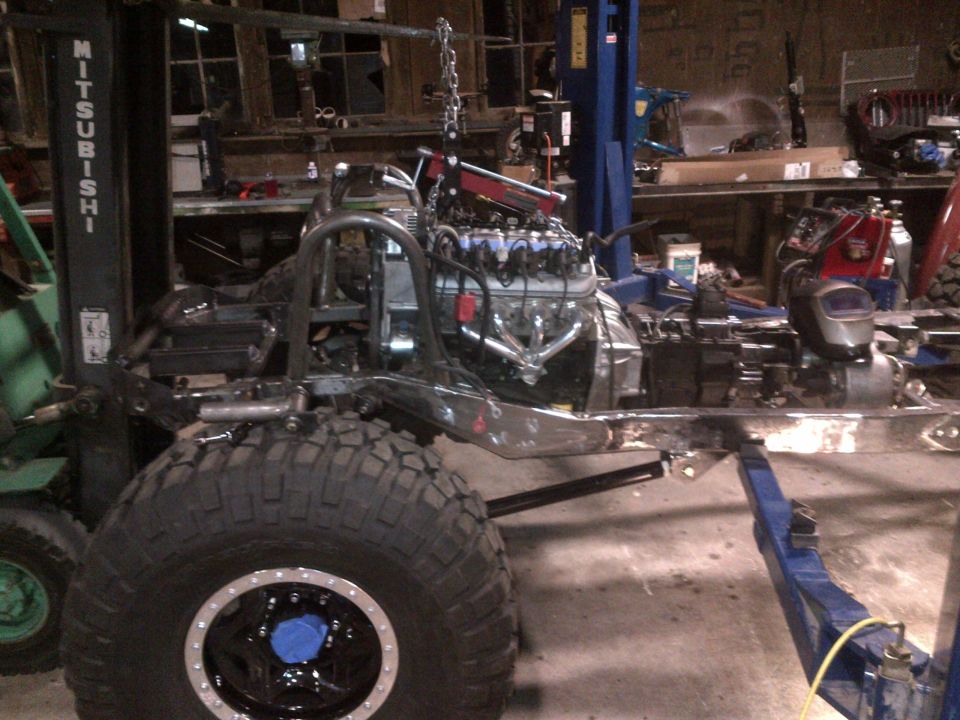Jeep CJ frame on lift with engine being installed. Forklift in background