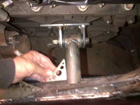 1985 Jeep CJ7 - A hand holds a metal bracket near the undercarriage of a vehicle, with visible engine components and welding.