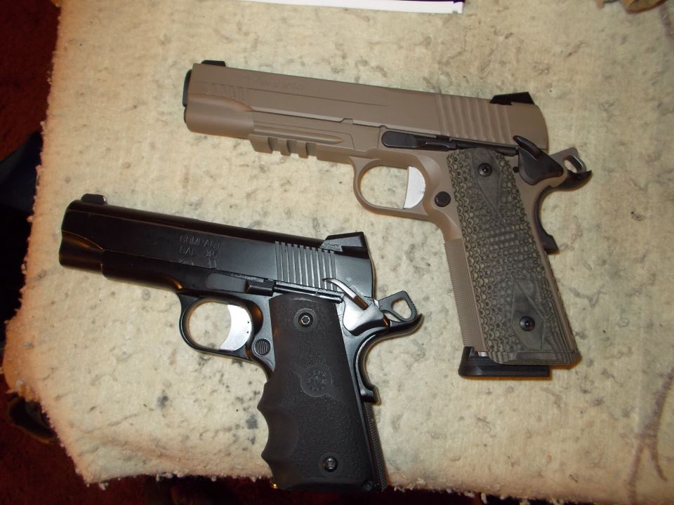 Two 1911-style pistols, one black and one tan, are shown side-by-side on a textured surface