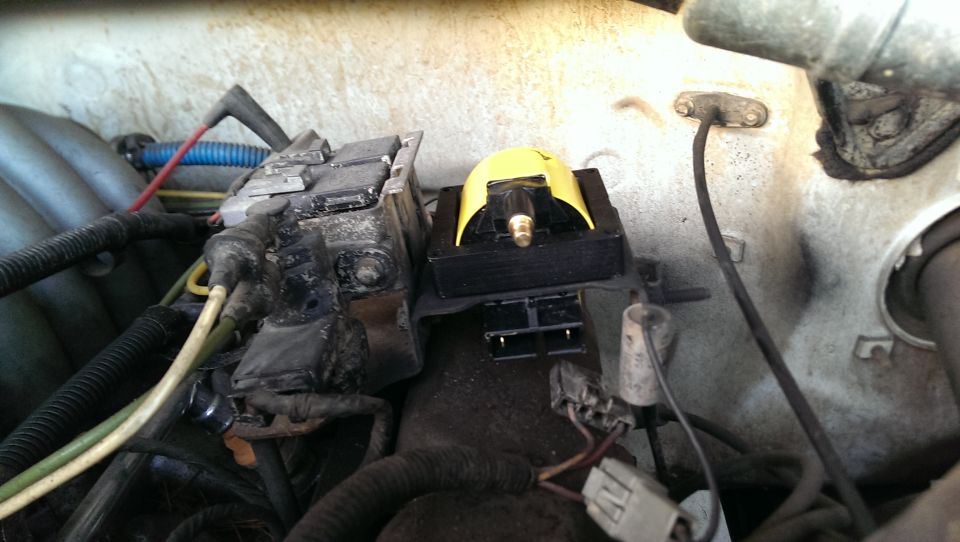 Yellow aftermarket ignition coil on bracket in engine bay with disconnected wiring connectors
