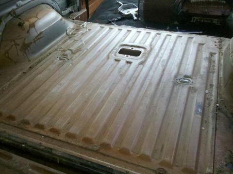 1982 Ford Bronco - The bare floor of a vehicle's cargo area shows a ribbed metal surface with tie-down points and some loose wiring.