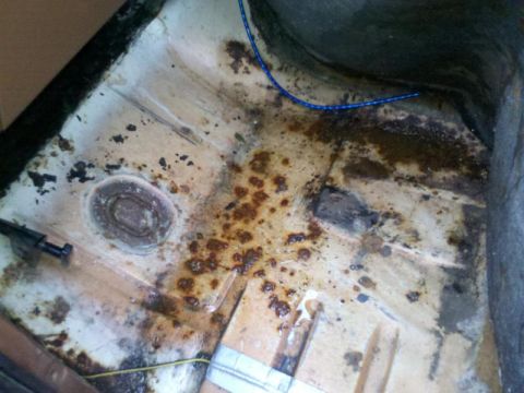 1982 Ford Bronco - The interior floor pan of a vehicle shows significant rust and dirt, with visible wiring and hardware.