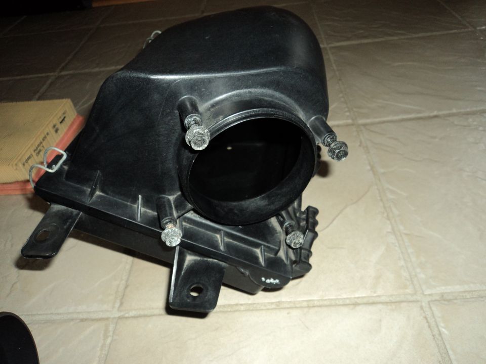Black plastic air intake box with bolts and an air filter next to it