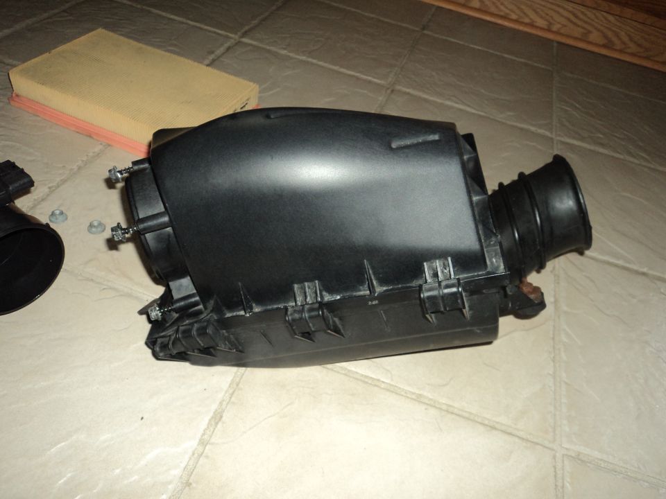 Black plastic air filter housing with intake hose and air filter on tiled floor