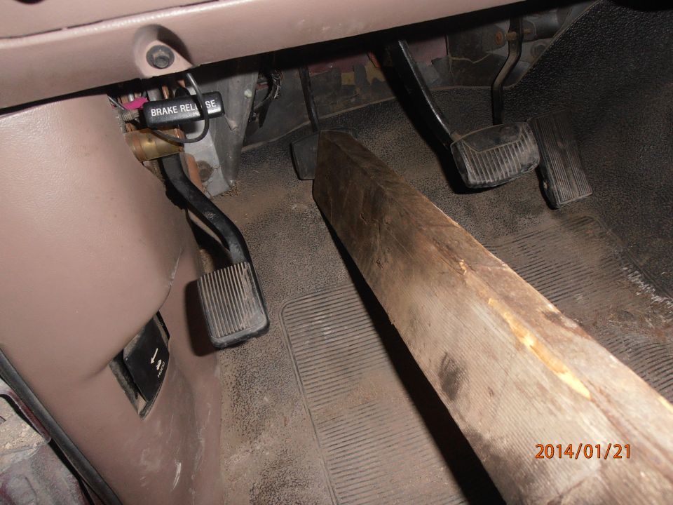 Vehicle interior showing brake and accelerator pedals, with a large piece of wood resting on the floor