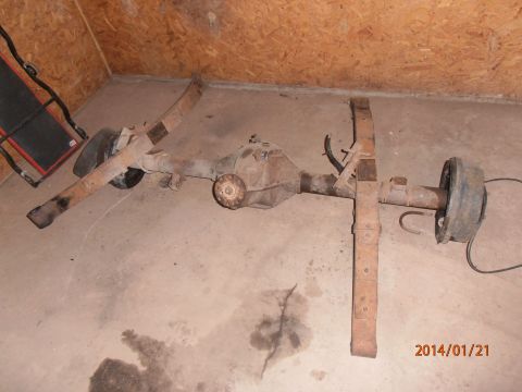 1996 Ford Bronco - A rusty rear axle assembly with leaf springs and brake drums is shown on a concrete floor.