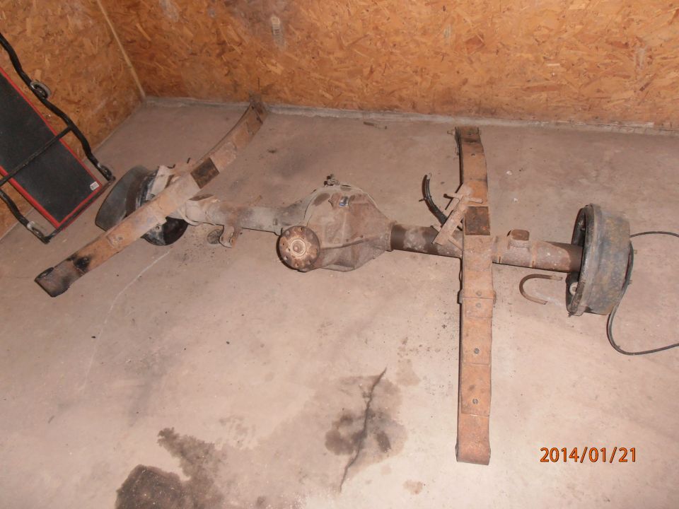 Rear axle assembly with leaf springs and brake drum, rusty, on concrete floor