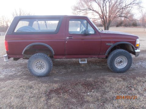 1996 Ford Bronco - This maroon Ford Bronco is shown from the side, with a spare tire visible through the rear window.
