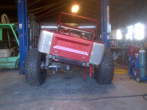 1985 Jeep CJ7 - This Jeep CJ is on a lift, showing its rear end with custom metal fenders and oversized tires.