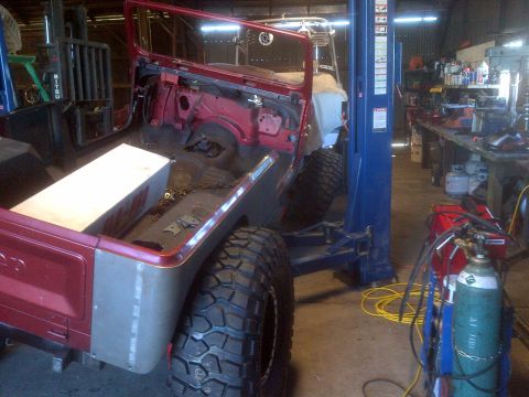 1985 Jeep CJ7 - A red Jeep CJ-series is elevated on a lift inside a workshop, undergoing repairs or modifications.