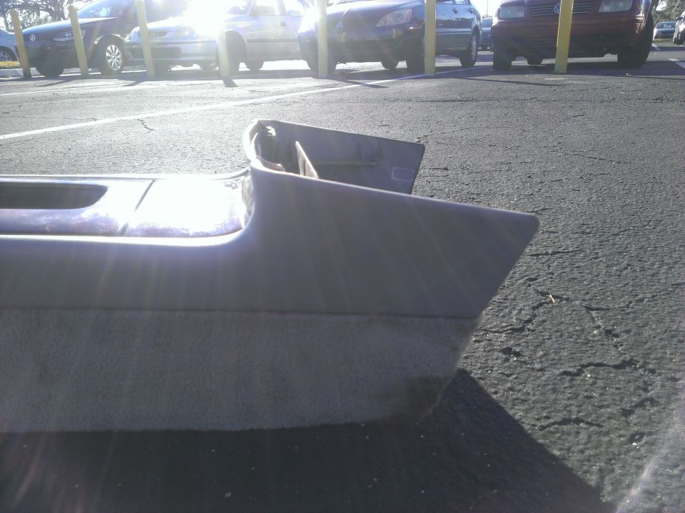 Gray plastic car interior trim piece with textured lower section, resting on asphalt