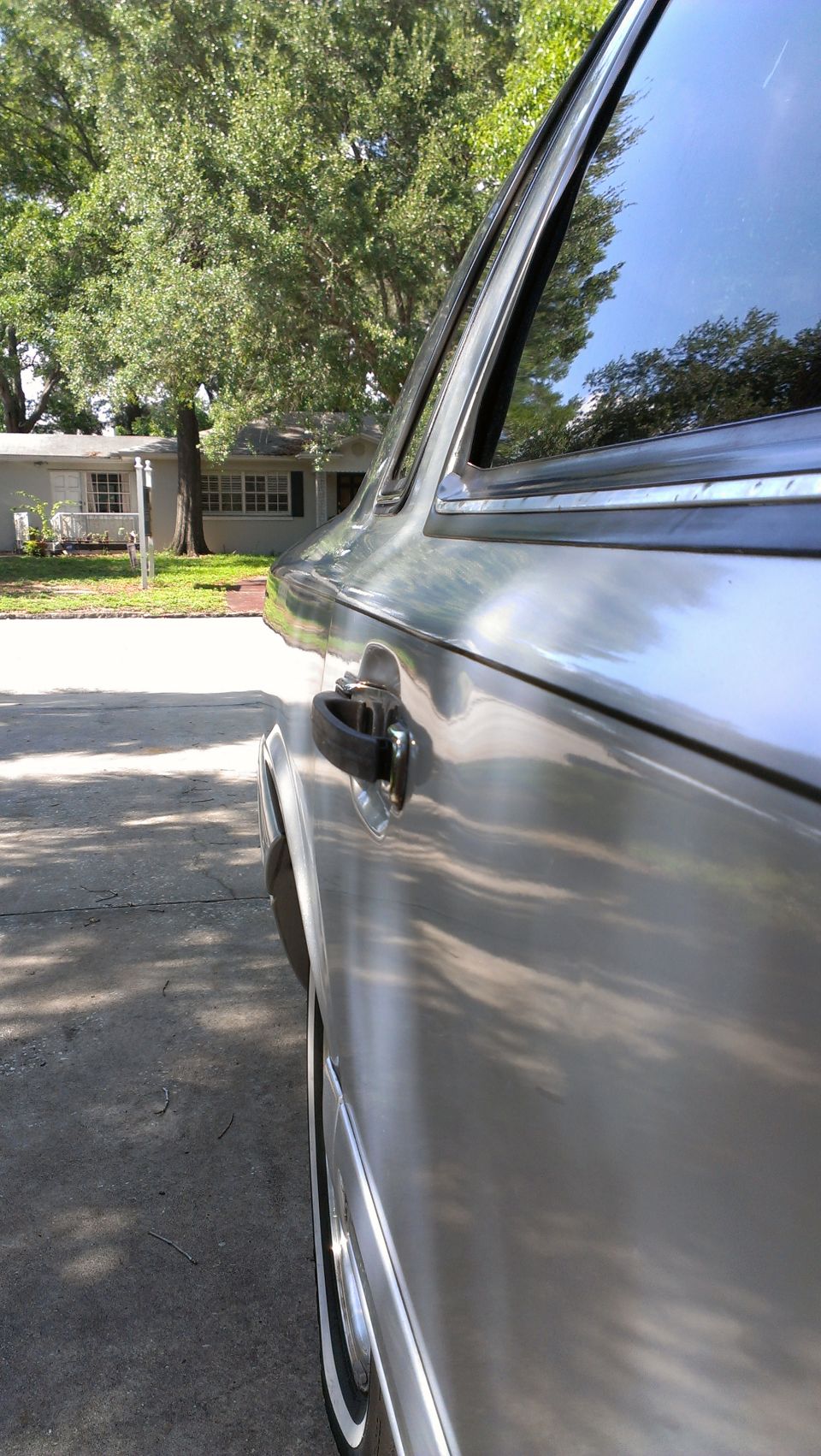 Side view of a silver sedan parked on a driveway, with a house and trees in the background