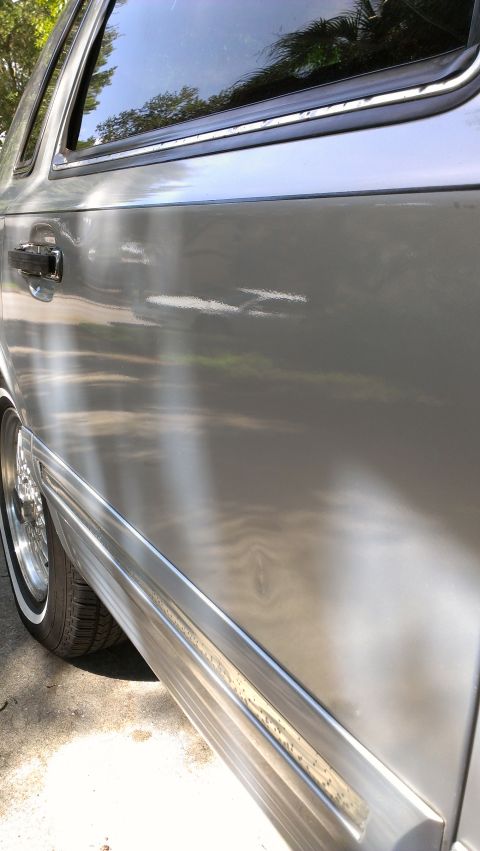 1996 Lincoln Town Car - Close-up of a silver car's side panel, showing the door handle and a portion of the wheel.