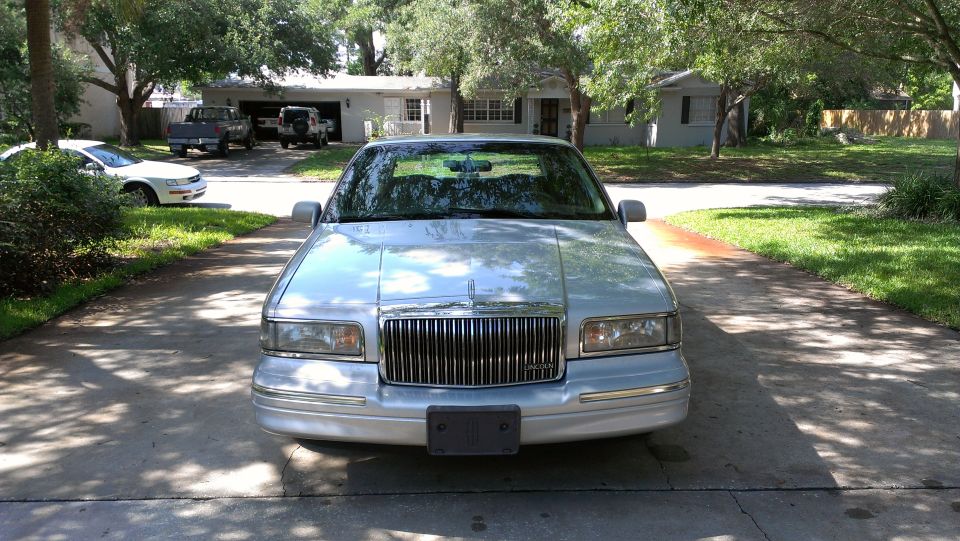 1995 Lincoln Town Car parked in driveway, front view. Two trucks and a white car are visible in the background