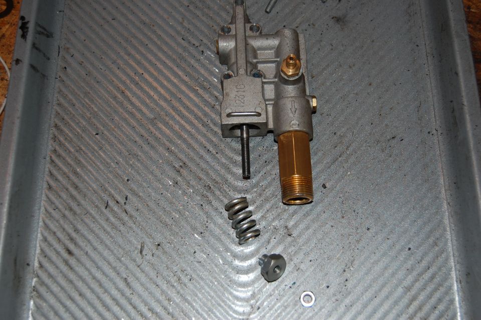 Disassembled pressure washer pump with spring and nut on a metal tray. Part number 1231C visible