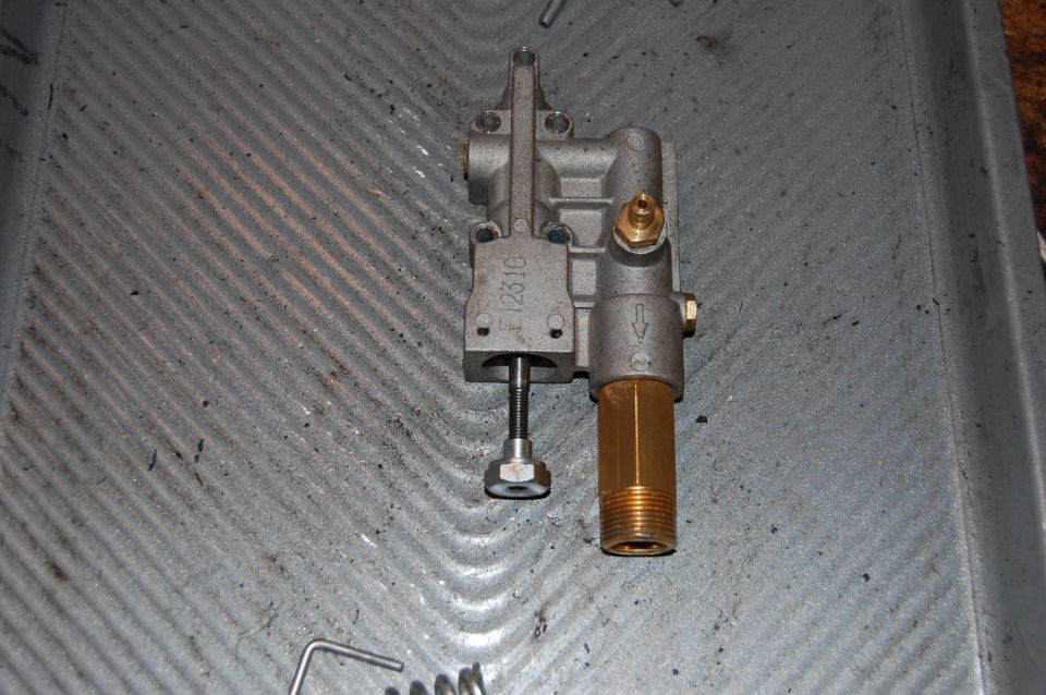 Metal valve assembly with brass fitting and threaded rod, resting on a ribbed surface