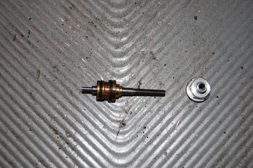 Metal valve stem with threaded end and a hexagonal nut on a textured gray surface