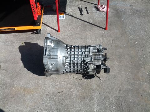 1989 BMW 3 Series - A GETRAG 260 transmission is shown resting on a concrete surface, with tools and a red stand in the background.