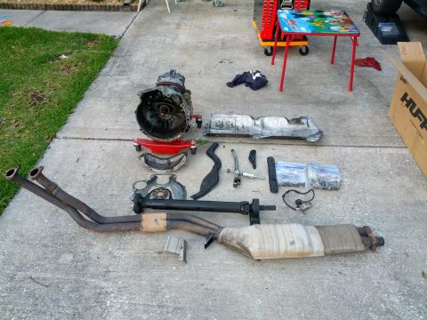 1989 BMW 3 Series - Various automotive parts are disassembled and arranged on a concrete surface, likely for repair or replacement.