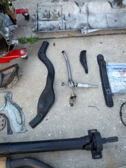 1989 BMW 3 Series - Various transmission and drivetrain components, including a shifter linkage and driveshaft, laid out on a concrete surface.