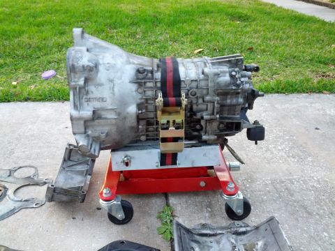 1989 BMW 3 Series - A Getrag transmission is shown mounted on a red, wheeled stand outdoors.