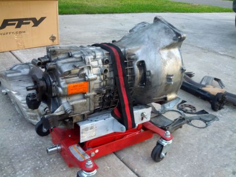 1989 BMW 3 Series - Transmission unit on a red jack, with a cardboard box and other parts nearby.