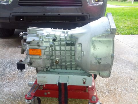1989 BMW 3 Series - A transmission is shown on a red rolling stand, with a portion of a gray SUV visible behind it.