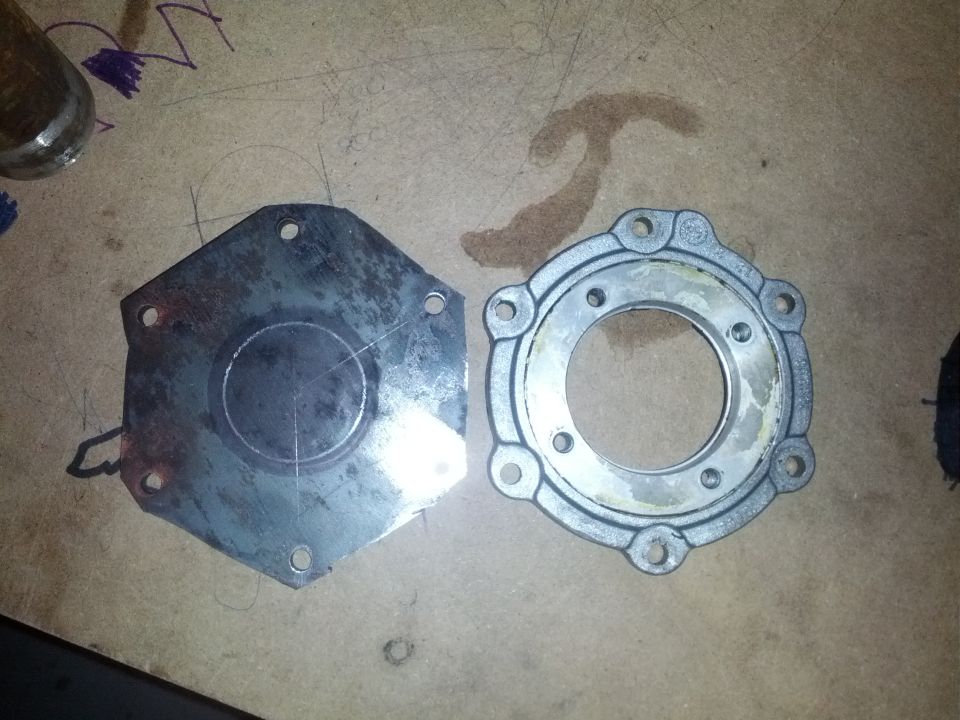 Two metal transmission parts on a wooden surface, one hexagonal and one circular with bolt holes