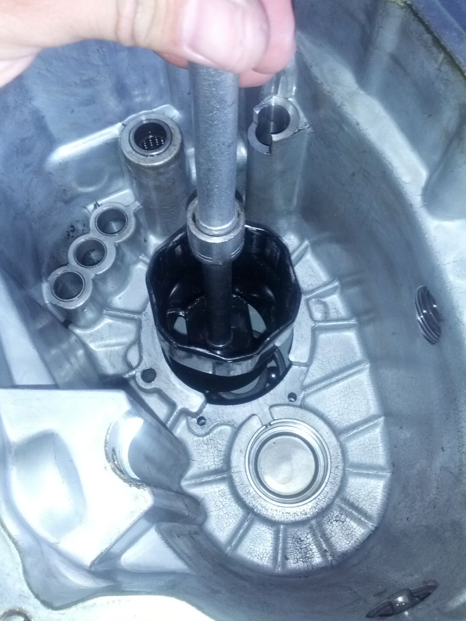 Using a tool to remove a black part from inside a metal transmission housing