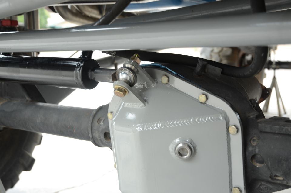 Close-up of a steering stabilizer and gray differential cover on a vehicle axle. Supermotors.net logo visible