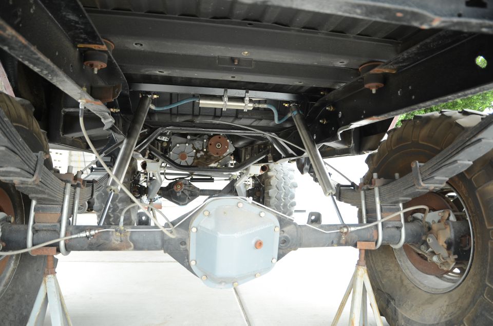 Underside view of a lifted 4x4 truck showing the rear axle, leaf springs, transfer case, and exhaust system