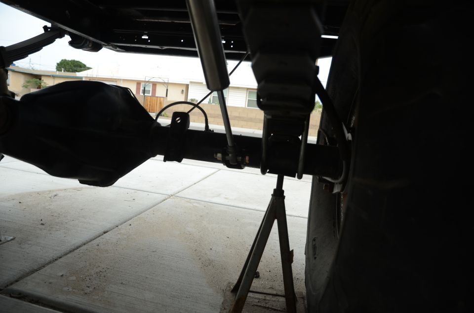 Close-up of a vehicle's rear axle, shock absorber, and leaf spring assembly supported by a jack stand