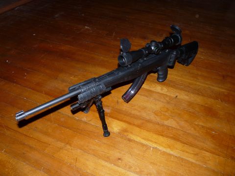 2006 Ford E350 - A rifle with a scope and bipod is displayed on a polished wooden floor.