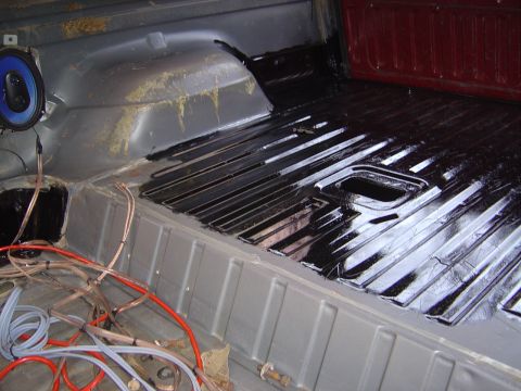 1986 Ford Bronco - The interior floor of a vehicle is being coated with a black protective substance, with wiring visible.