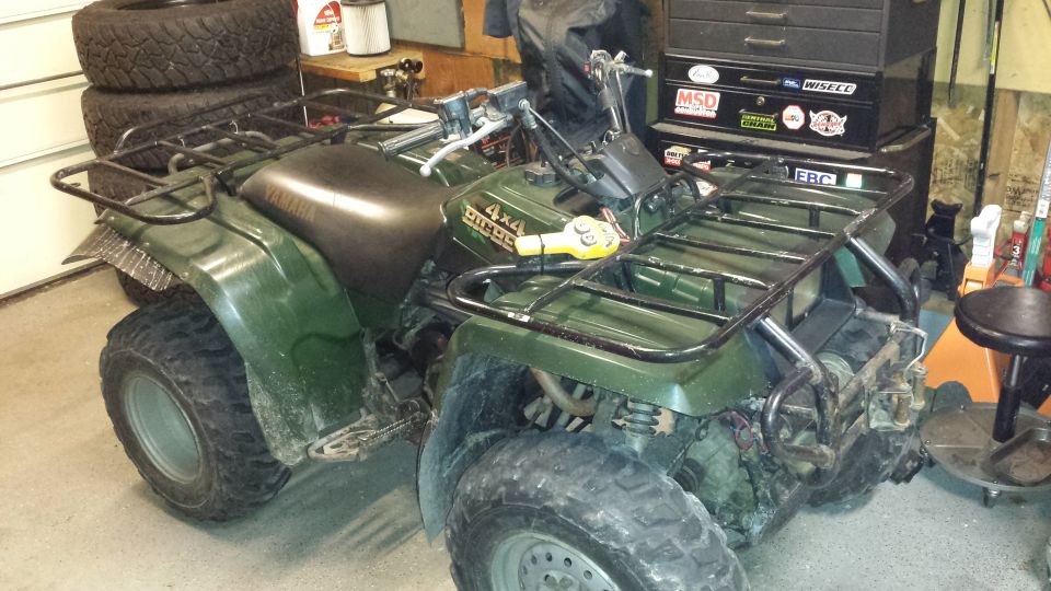 Green Yamaha Big Bear 4x4 ATV with black racks parked in a garage next to tool chests