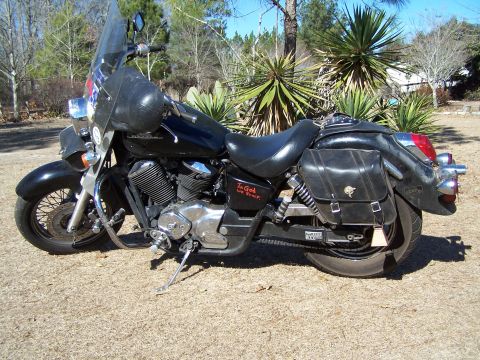 1998 Honda Shadow VT750C - A black motorcycle with saddlebags and a windshield is parked outdoors. The phrase 'In God We Trust' is visible on the side of the motorcyc…