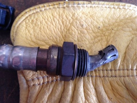 2010 Dodge Challenger - An oxygen sensor with a bent tip rests on a piece of yellow leather. The Supermotors.net logo is visible in the lower right corner.