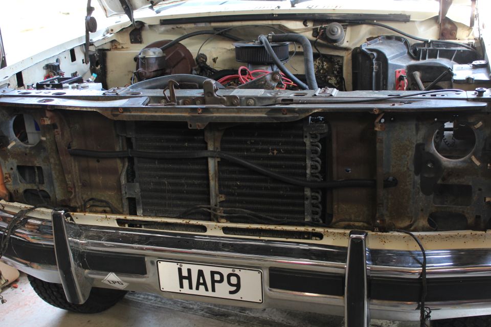 Front of white Bronco with grille and headlights removed, exposed radiator area, chrome bumper with HAP9 plate