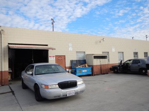 2003 Ford Crown Victoria - silver four-door sedan and a dark SUV with open door sit in front of a beige industrial building with open shop bays.