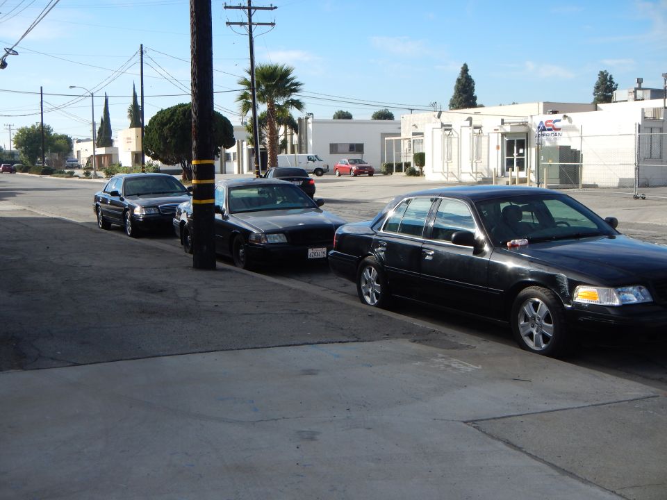 Row of dark sedans parked along a curb beside an industrial street