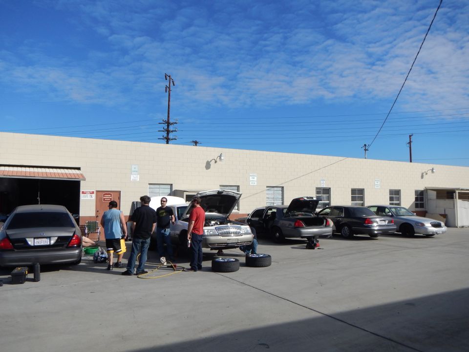 Row of sedans with open hoods being serviced outside an industrial shop