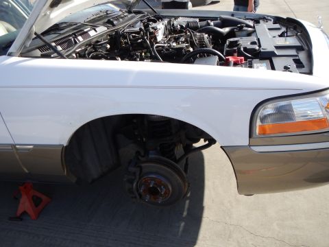 2003 Ford Crown Victoria - Close-up of a two-tone car's front corner with the fender removed, exposing the engine bay, suspension, and bare brake rotor hub.