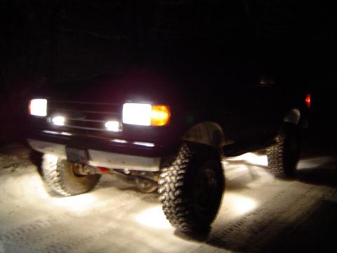 1989 Ford Bronco - A 1989 Ford Bronco is seen driving through snow at night, its headlights illuminating the snowy path ahead.