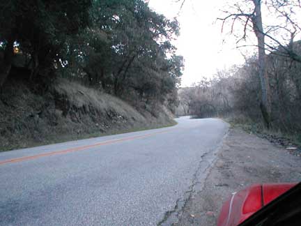 1994 Ford Crown Victoria - A road winds through a wooded area under a bright sky. A red vehicle is visible in the lower right corner.